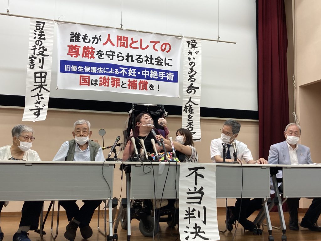 神戸地裁判決後の原告集会 登壇する夫妻（左から妻、夫）＜2021年8月3日 神戸市内＞