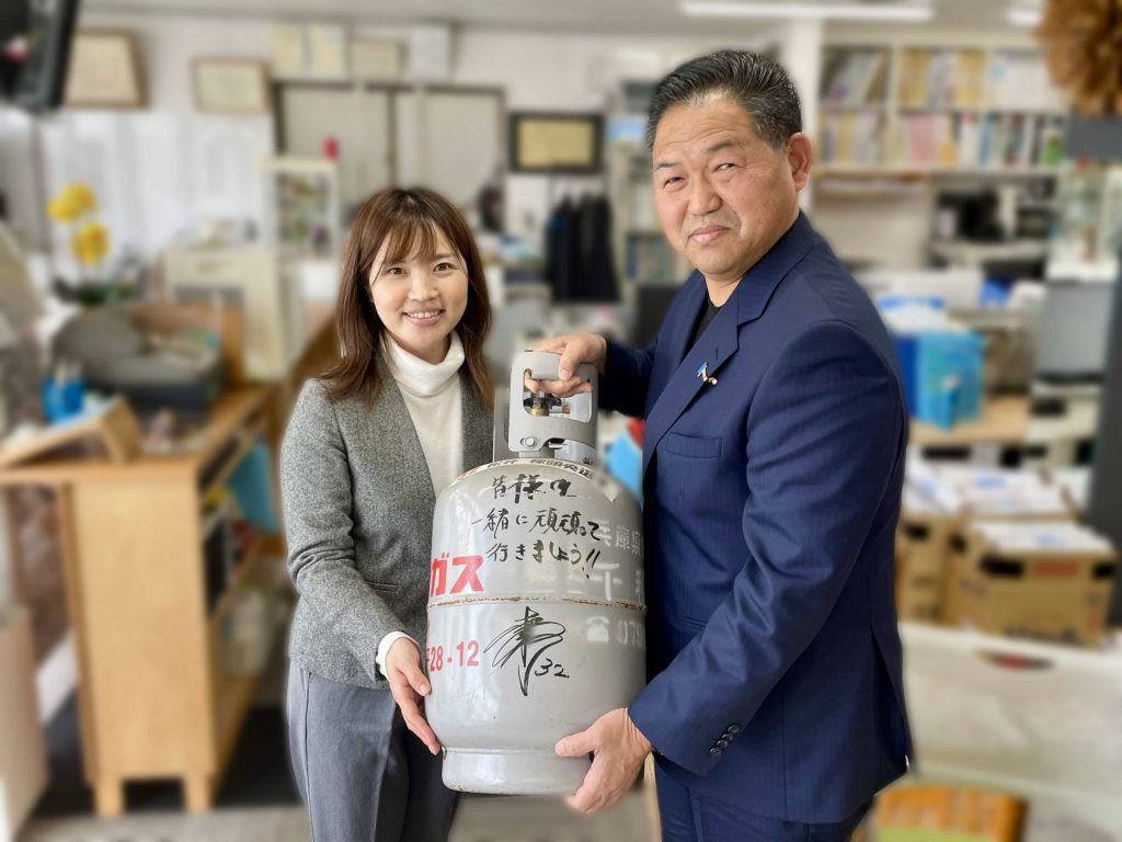 被災地に持参したLPガスボンベ　松井稼頭央選手のサインとメッセージ入り　写真右：兵庫県LPガス協会・西播西支部副支部長の千種和英さん、左：番組パーソナリティの小倉実華さん